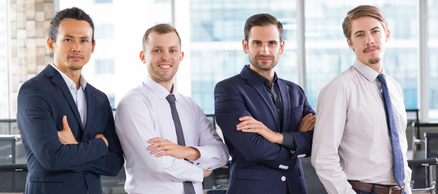 Four businessmen standing in a line together with their arms crossed in an office.