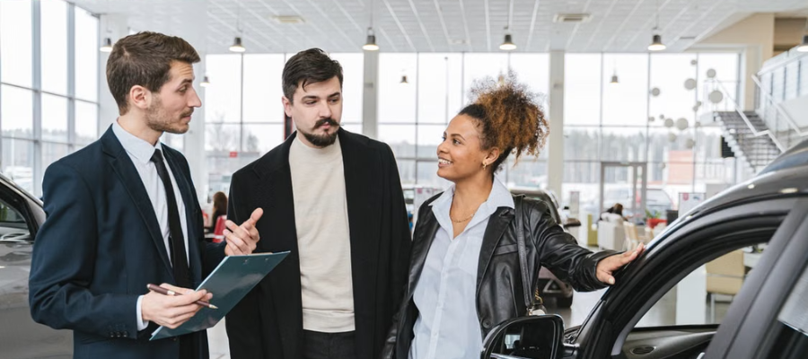 man and woman standing at car inside dealership with male sales associate